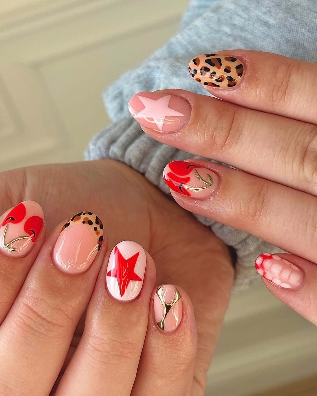 Bold red nails with cherries, leopard print, stars, and golden wire accents for a playful mixed design.
