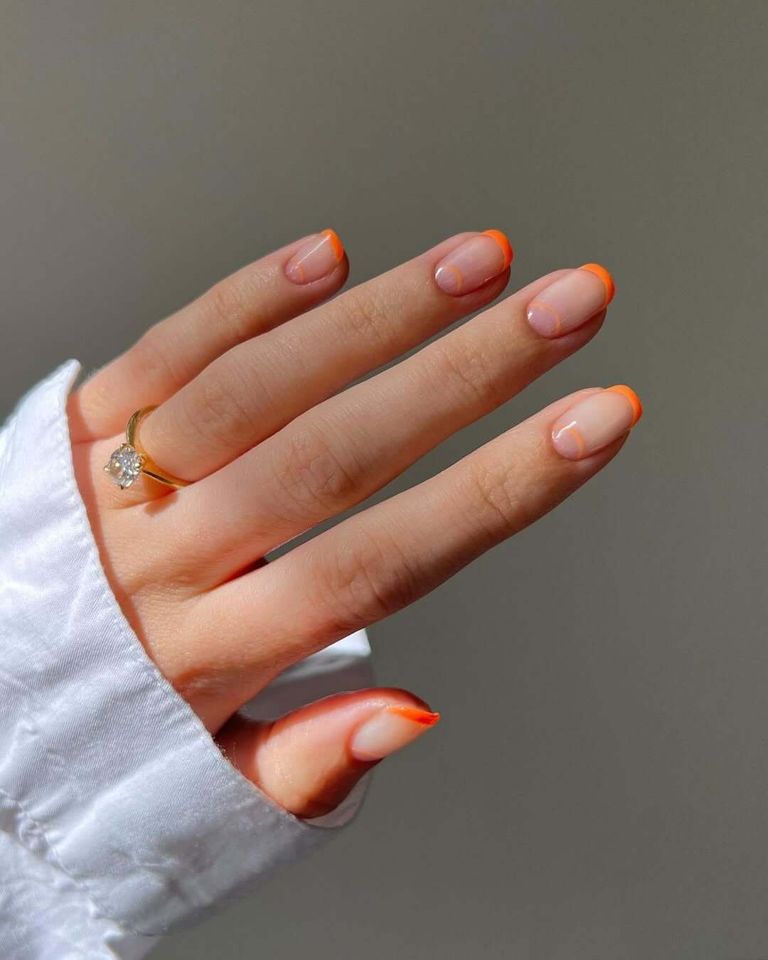 Short oval nails with nude bases and bright orange French tips for a fresh and playful finish.