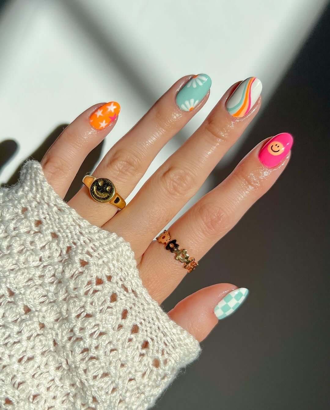 Short gel nails with smiley faces, pastel swirls, and checkered tips for a colorful retro vibe.
