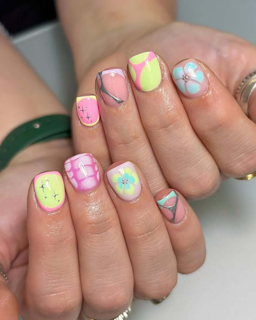 Short gel nails with pastel florals, 90s-style swirls, and sparkly accents for a playful, artistic finish.