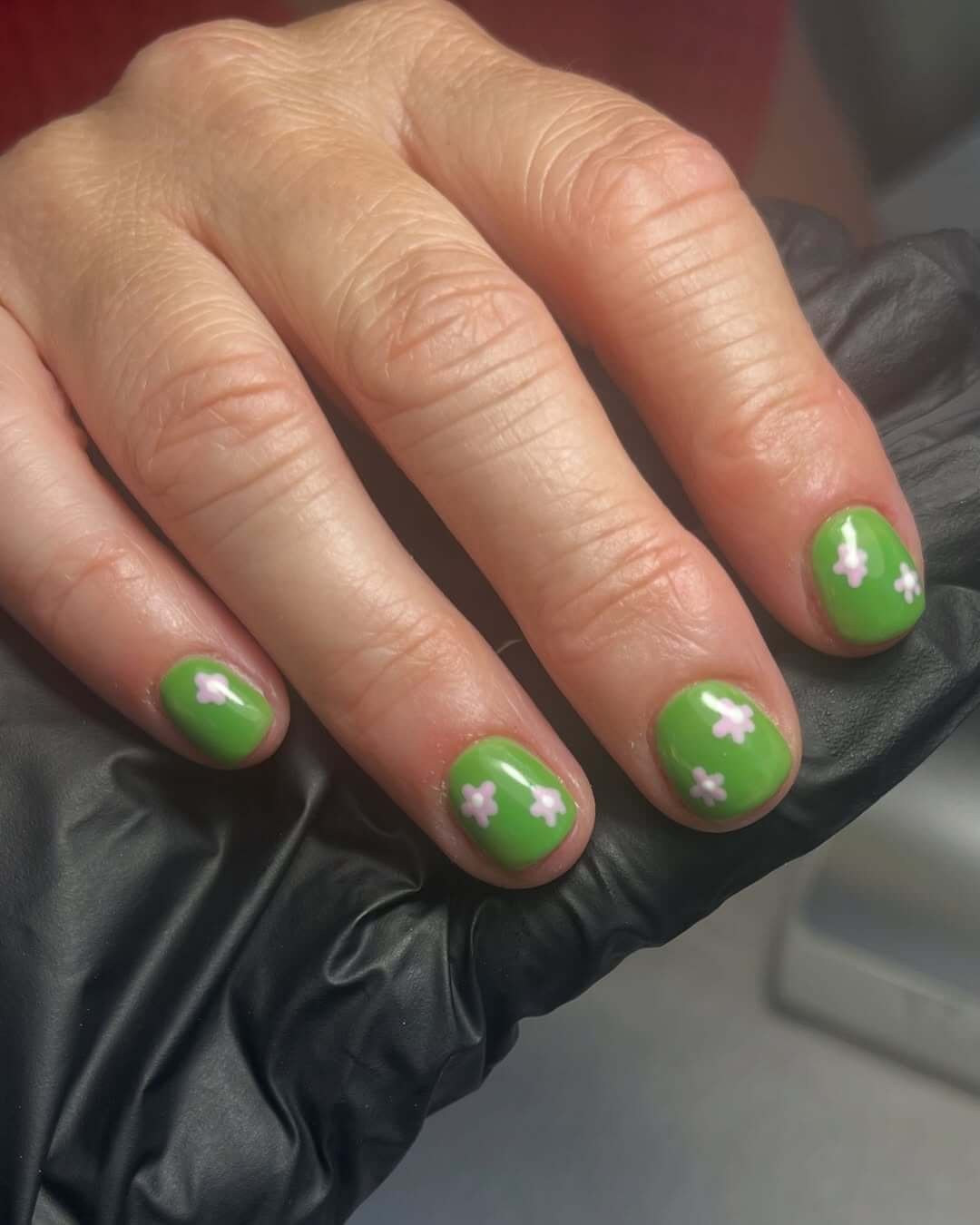 Short green nails with tiny pink and white floral designs inspired by a blooming meadow.