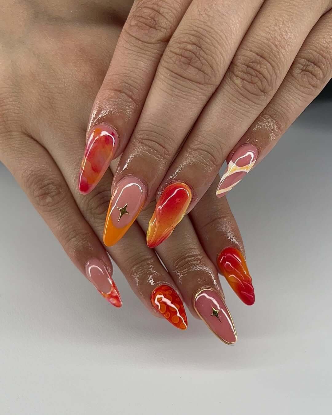 Almond red nails for summer with fiery orange, pink, and red swirl design and a glossy finish.