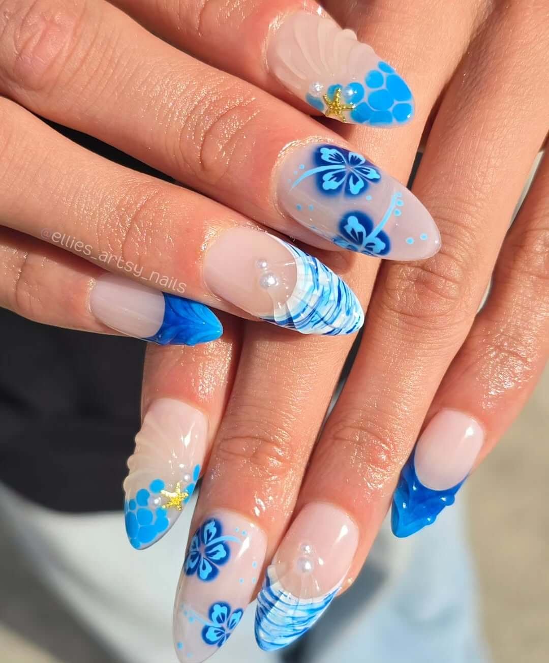 Almond nails with blue hibiscus art, shell tips, pearl accents, and ocean textures.