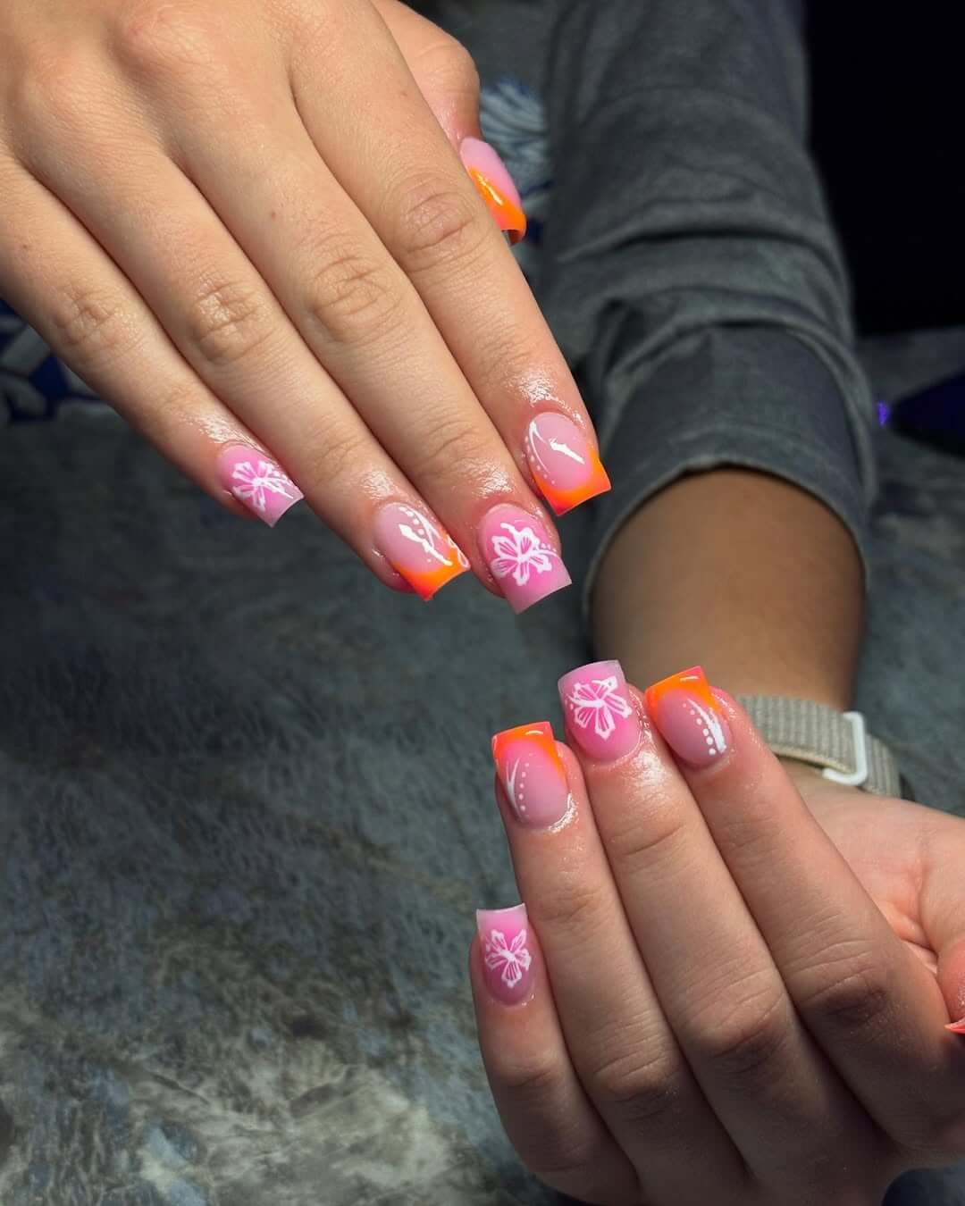 Square short nails with orange-pink ombré French tips and white hibiscus flowers for a tropical sunset effect.