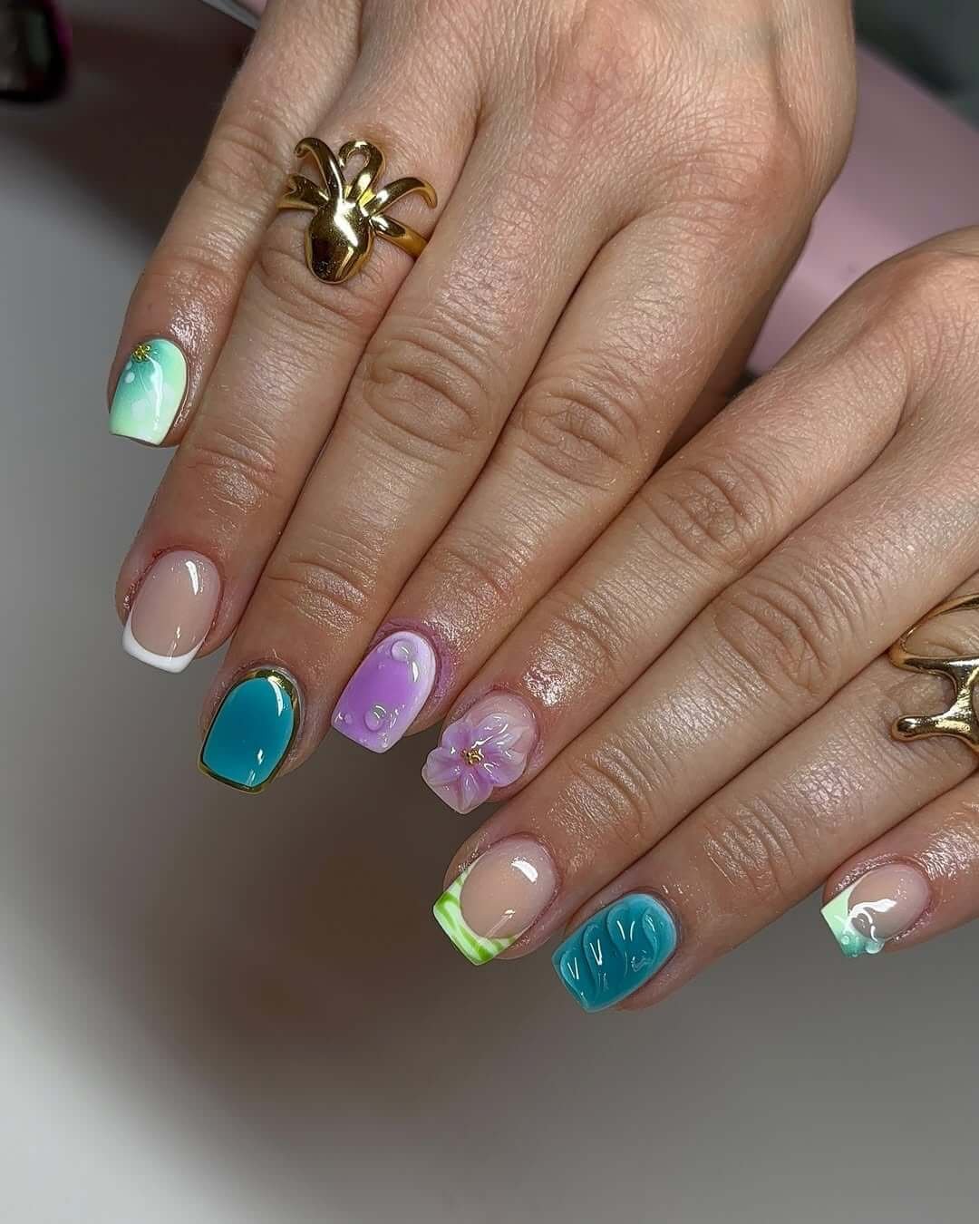 Square short nails with mint gradients, ocean blue polish, and 3D floral accents for a lush island-inspired design.