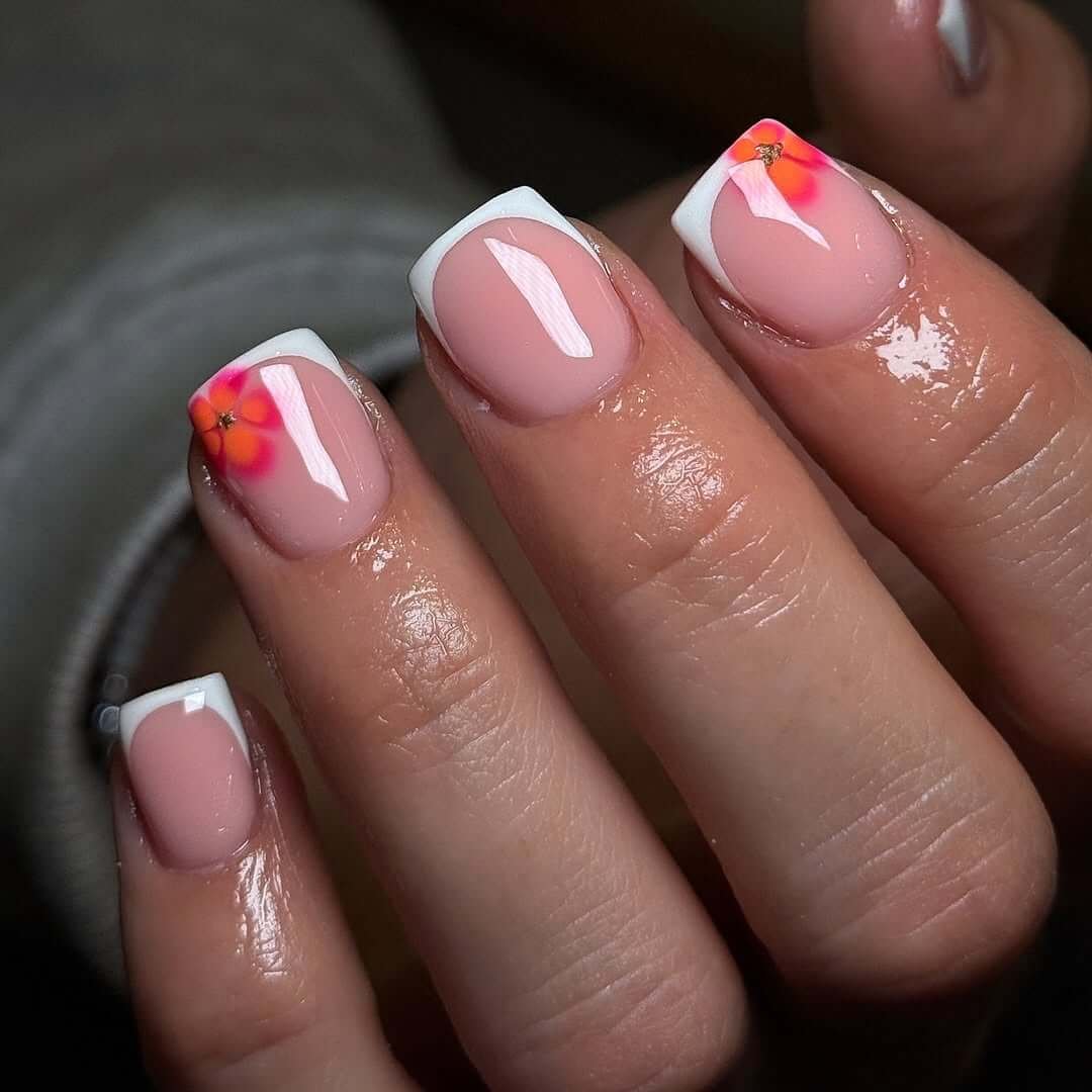 Short French tip nails with neon orange-pink floral accents for a bright and playful take on the classic.