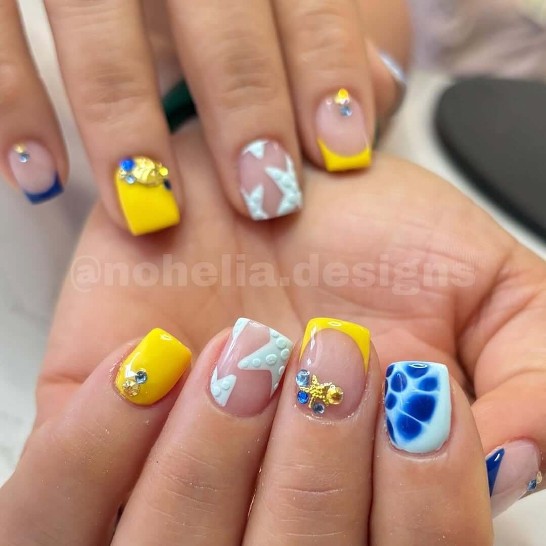 Nails in bright yellow and blue with starfish, bubbles, and gems for a textured ocean fantasy.