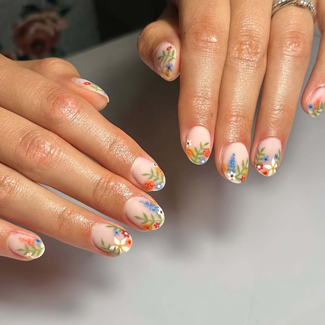 Almond nails with soft nude base and delicate wildflower accents for a romantic garden-inspired manicure.