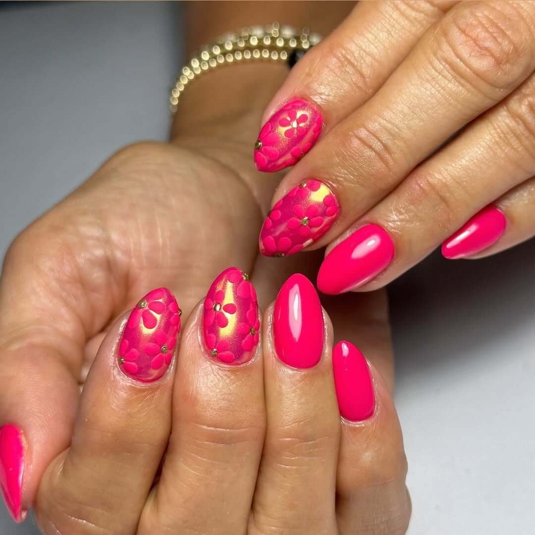 Almond nails in hot pink with embossed floral art and golden chrome accents for a bold glam finish.