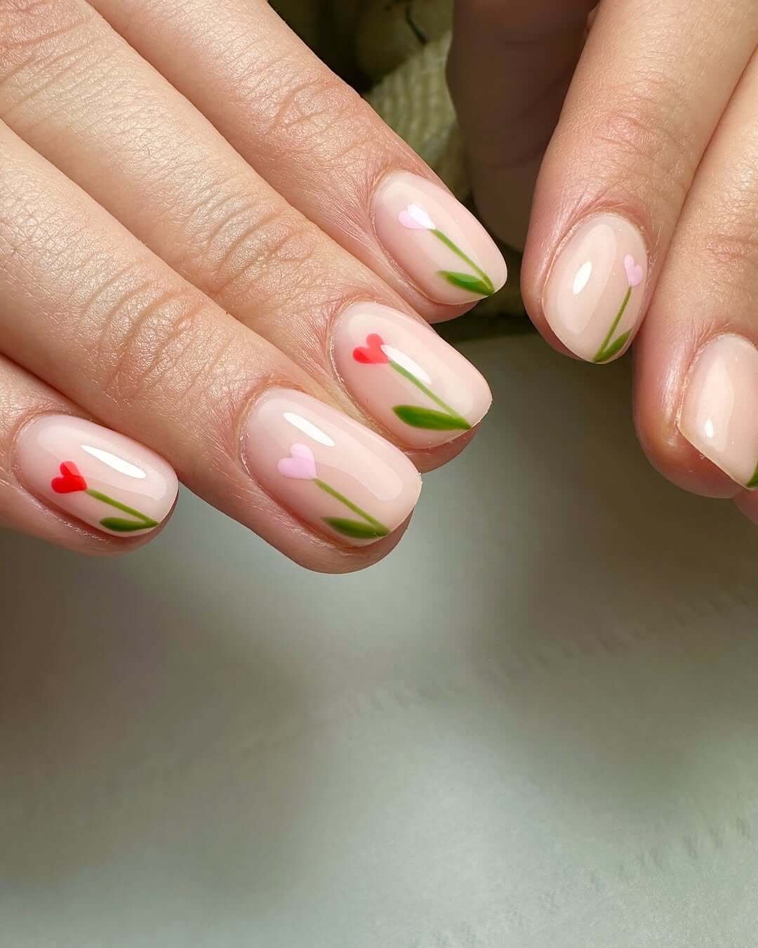 Almond-shaped biab nails with tiny heart-shaped flowers and green stems on a nude base for a sweet minimalist design.