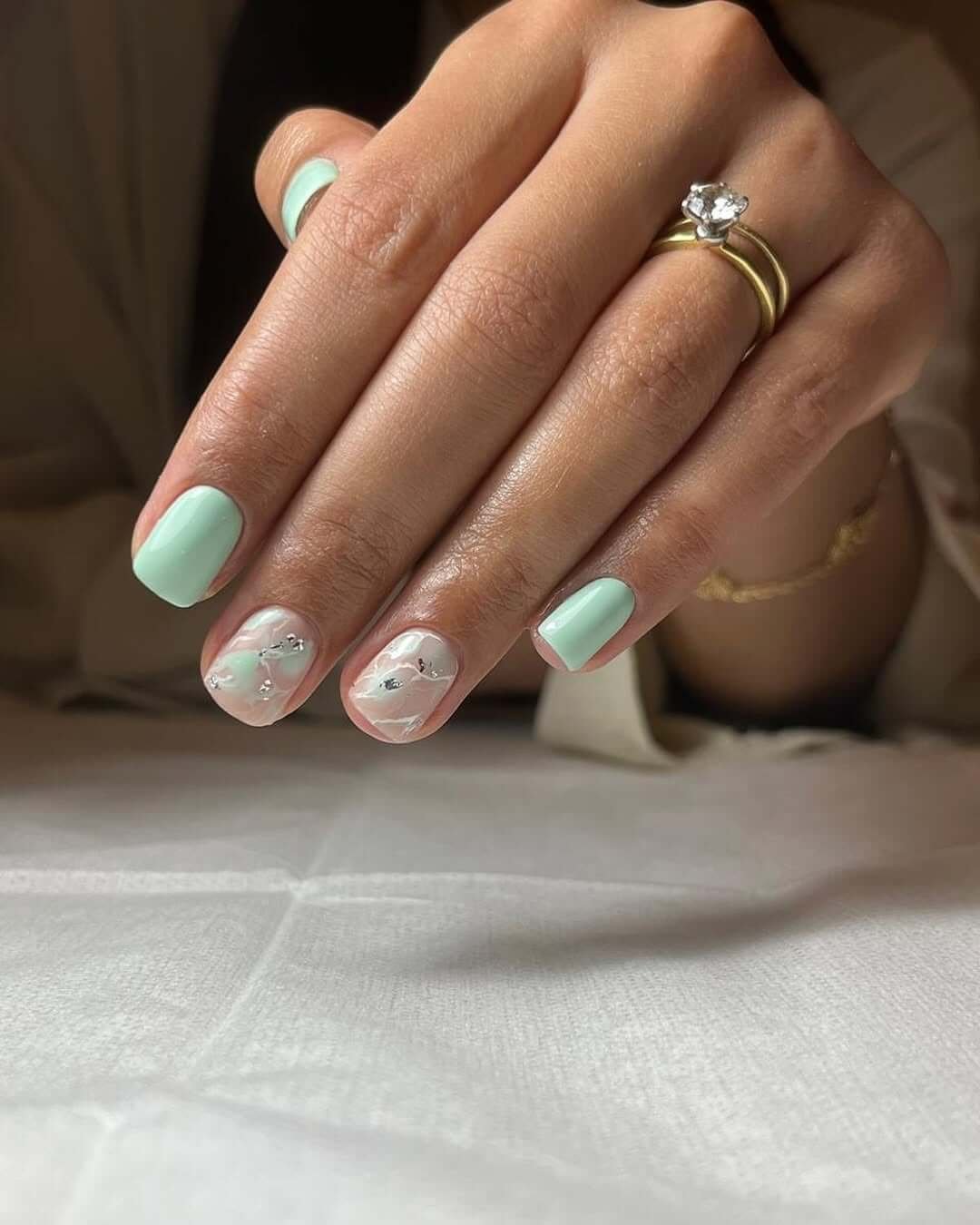 Short nails in soft mint polish with sheer marble accents and silver foil for a refined, minimalist look.